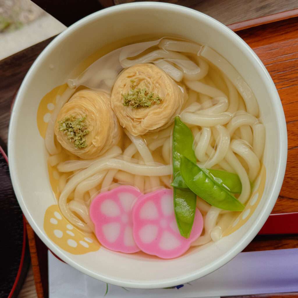 A bowl of udon noodle soup with rolls of tofu to try on a day trip to nikko