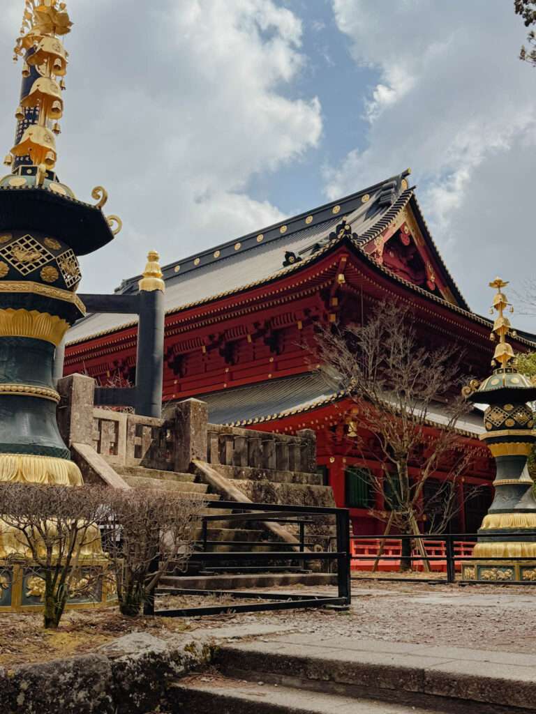 Looking up towards a red temple flanked by decorative black and gold pillars as part of the Rinnoji Temple of Nikko
