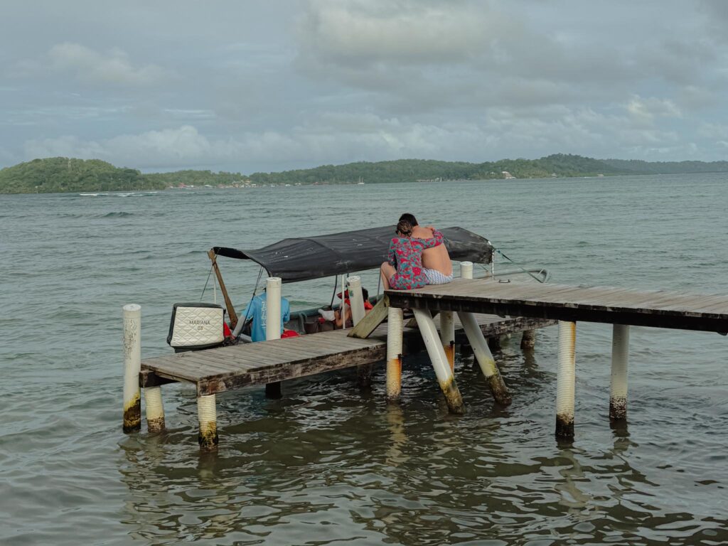 A wooden dock in Bocas del Toro with a boat moored alongside, looking out over the Caribbean sea toward a forested island in the distance