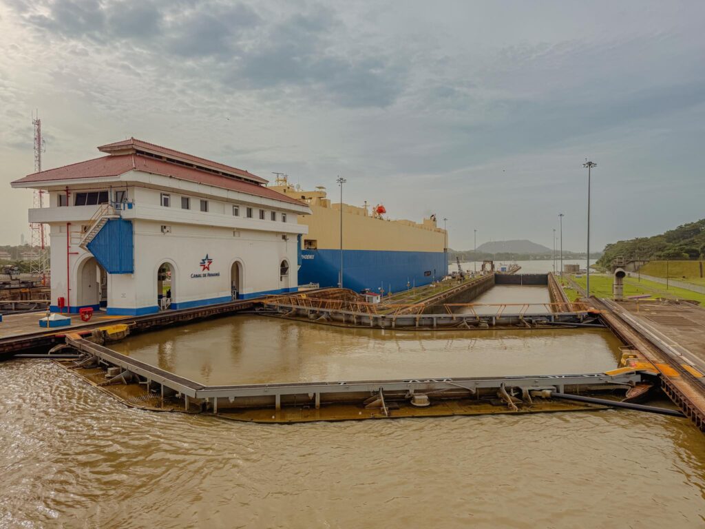A large vehicle carrier filling the Miraflores lock chamber viewed from a boat at water level during a Panama Canal partial transit