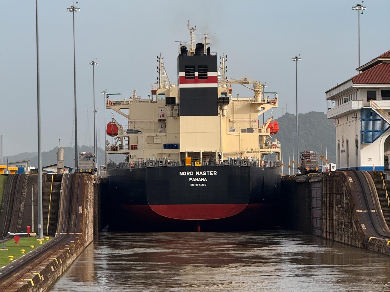 The bulk carrier Nord Master entering a Panama Canal lock head-on, with the lock walls rising on either side and the Miraflores control building visible to the right
