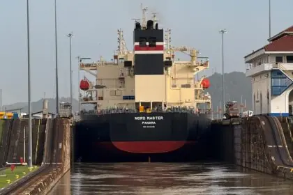 The bulk carrier Nord Master entering a Panama Canal lock head-on, with the lock walls rising on either side and the Miraflores control building visible to the right