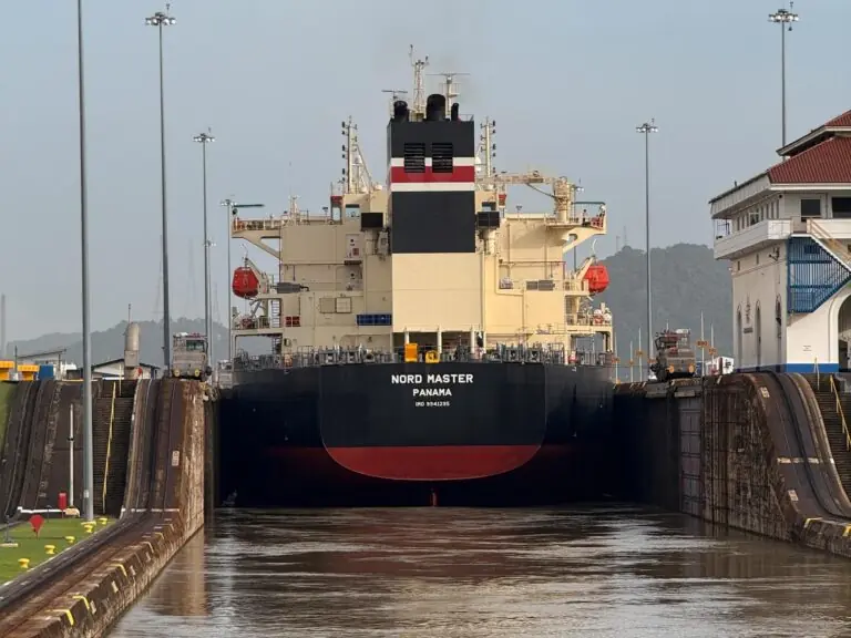 The bulk carrier Nord Master entering a Panama Canal lock head-on, with the lock walls rising on either side and the Miraflores control building visible to the right