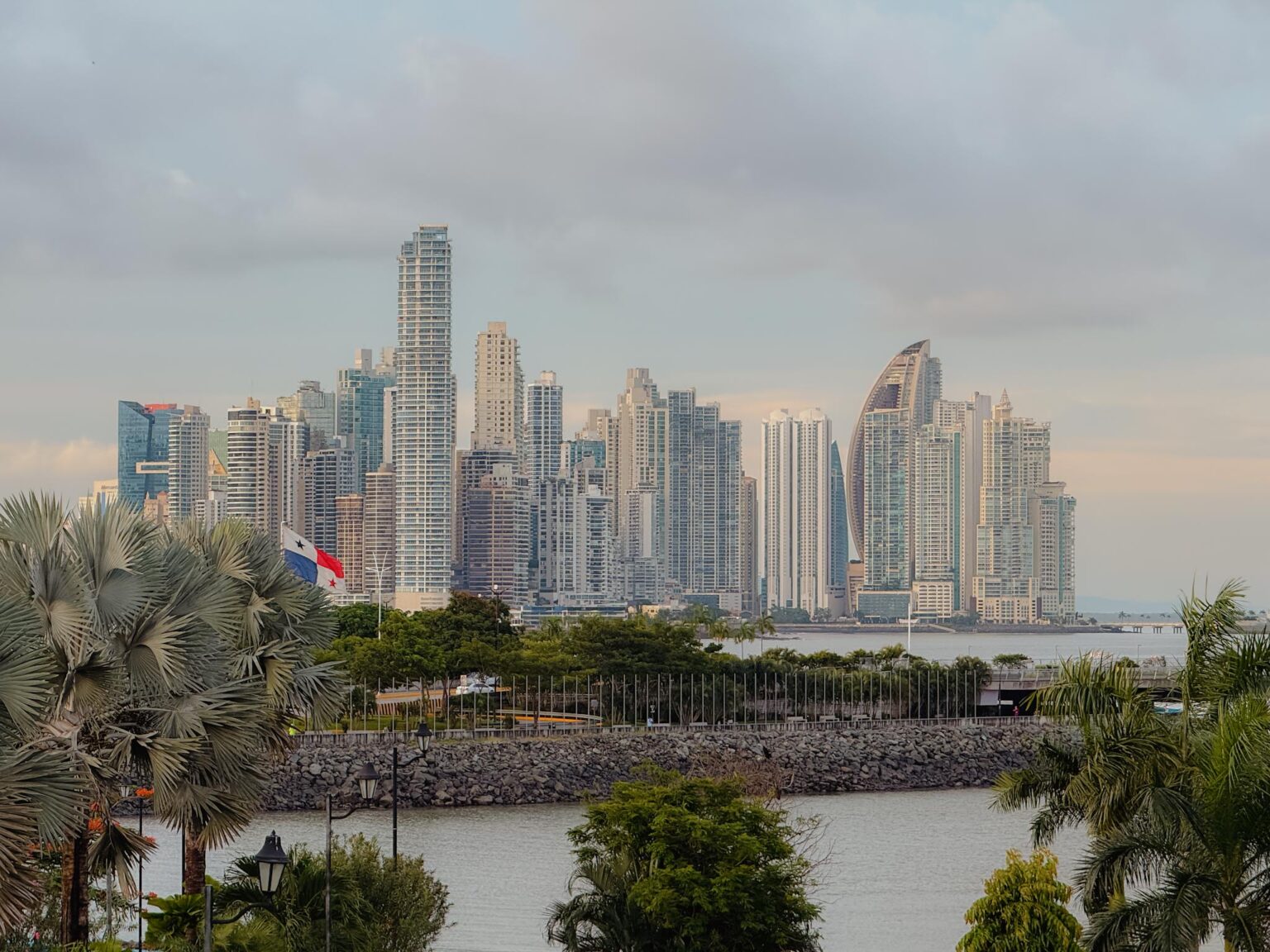 Panama City skyline viewed from Casco Viejo, with the Panamanian flag in the foreground and skyscrapers rising along the Pacific waterfront