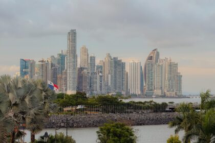Panama City skyline viewed from Casco Viejo, with the Panamanian flag in the foreground and skyscrapers rising along the Pacific waterfront