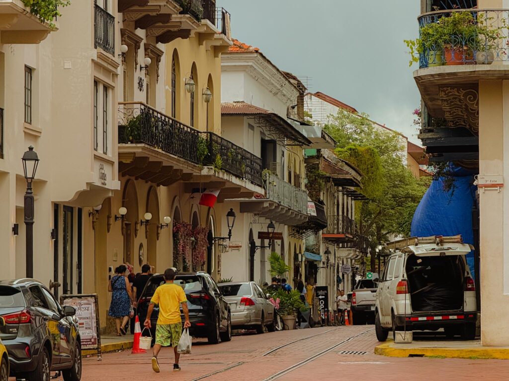Colonial street scene in Casco Viejo, Panama City, with wrought iron balconies, arched doorways, and locals walking along the cobblestone road