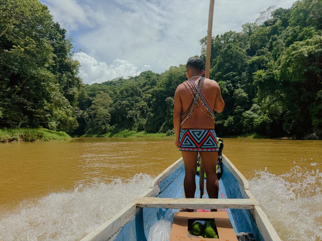 Embera guide standing at the bow of a traditional wooden canoe on the Chagres River, Panama, surrounded by dense rainforest