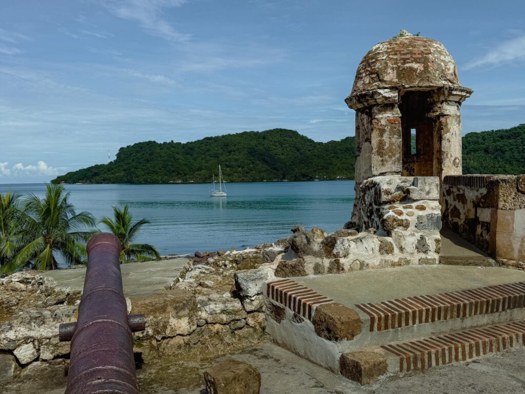 Spanish colonial cannon and watchtower at the Portobelo forts, with the Caribbean Sea and Isla Grande visible in the background