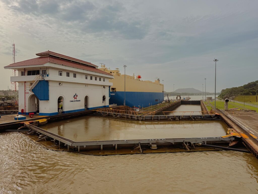 Large cargo ship passing through the Miraflores Locks on the Panama Canal, with the Canal de Panama control building in the foreground