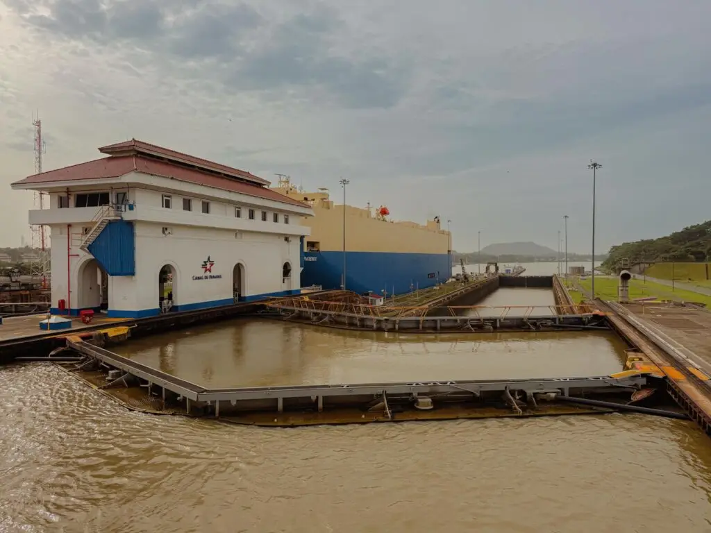 Large cargo ship passing through the Miraflores Locks on the Panama Canal, with the Canal de Panama control building in the foreground