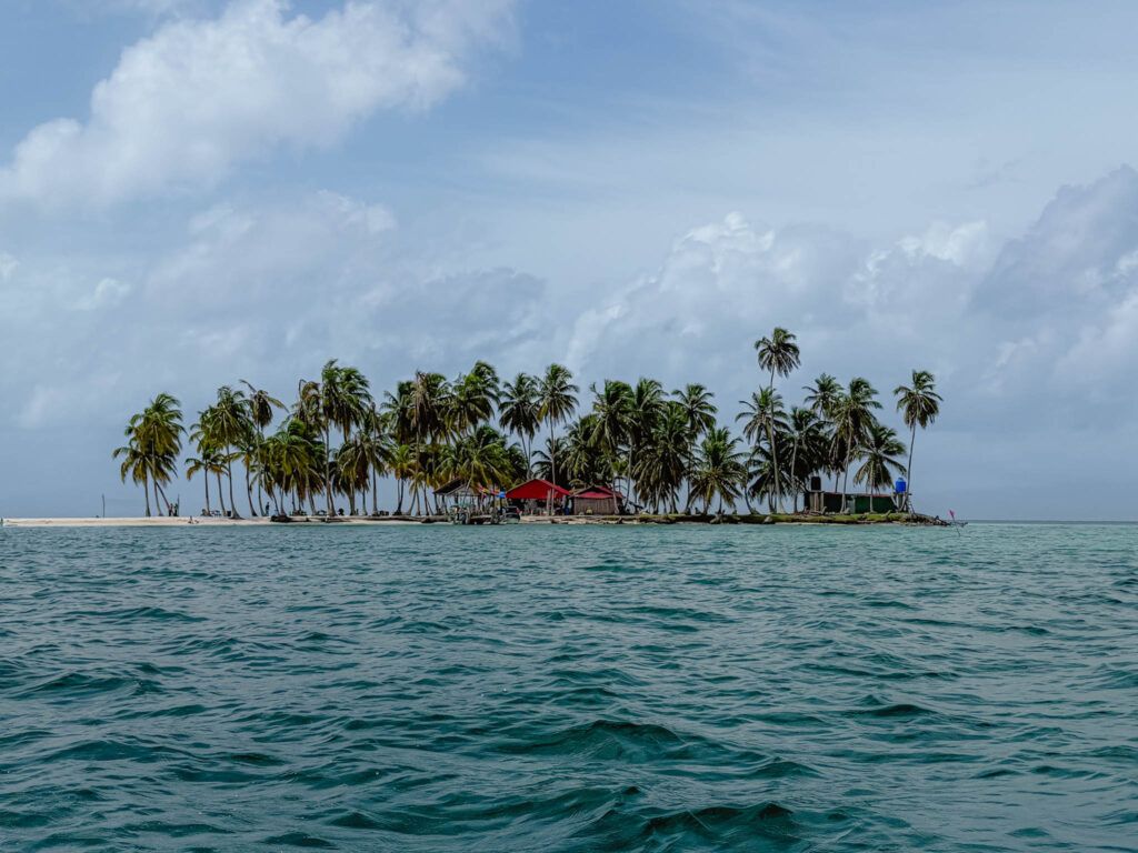 A small Guna Yala community island in the San Blas archipelago surrounded by open water and lined with palm trees, Panama -- day trips from Panama City