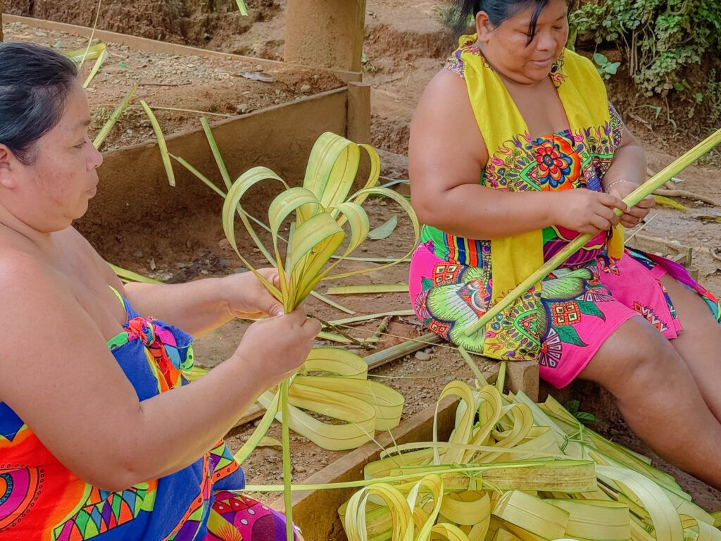 Two Embera women in traditional dress weaving palm fronds at an indigenous community in the Panama rainforest -- day trips from Panama City