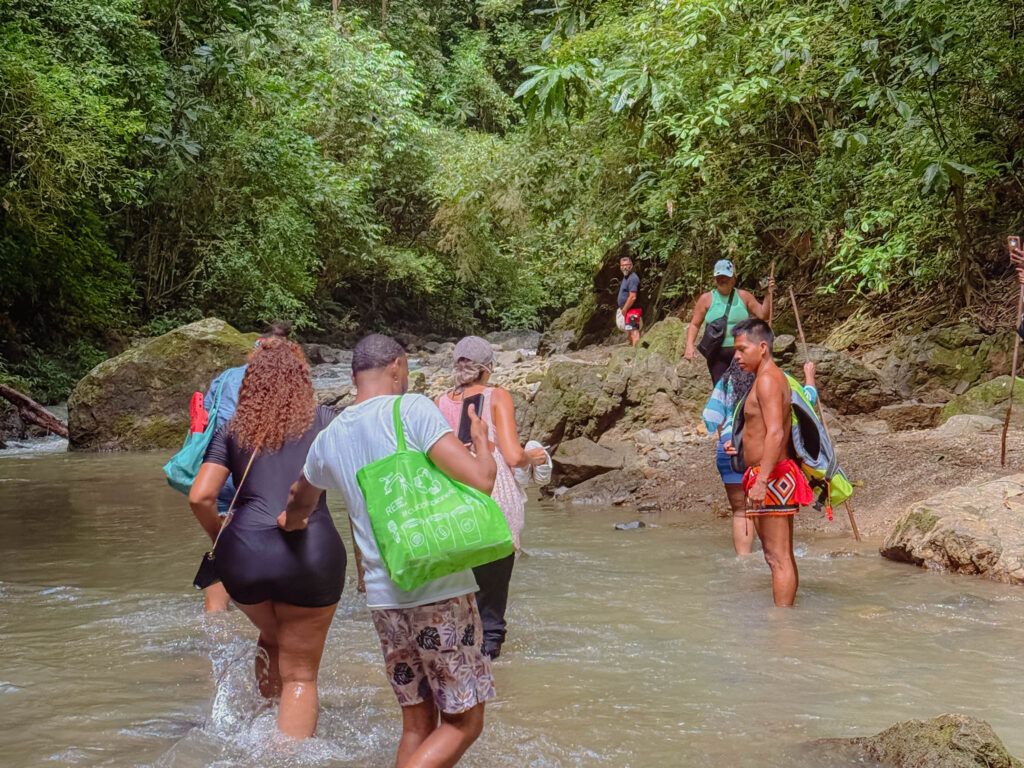 Group of visitors wading through a rocky jungle river with an Embera guide on the waterfall hike, Panama rainforest -- day trips from Panama City