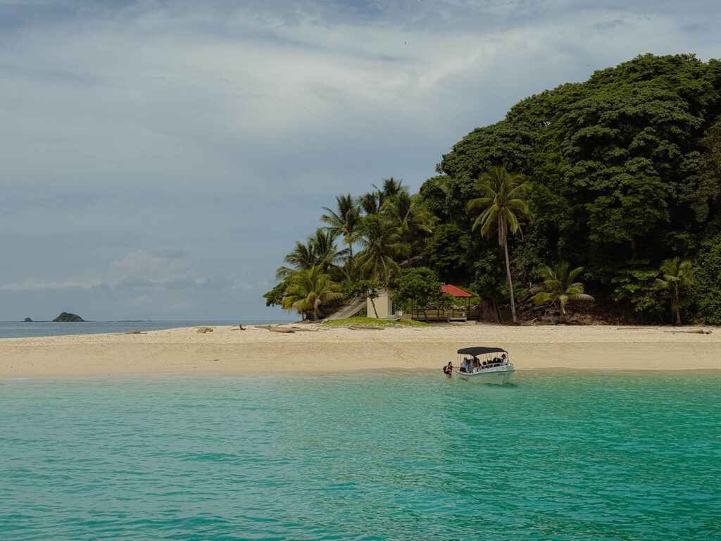 Small tour boat arriving at a white sand beach on a Pearl Island with turquoise Pacific water and dense jungle, Panama -- day trips from Panama City