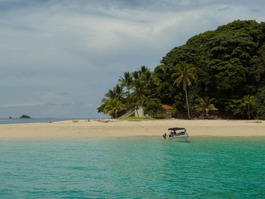 Small tour boat arriving at a white sand beach on a Pearl Island with turquoise Pacific water and dense jungle, Panama -- day trips from Panama City