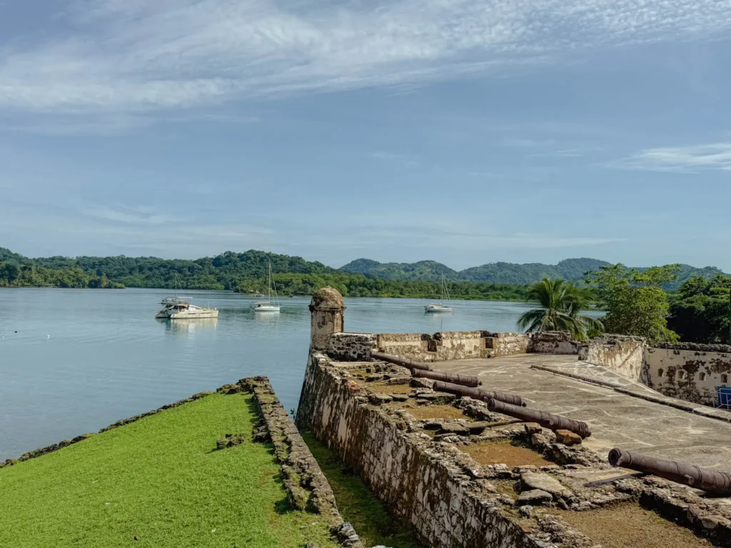 Spanish colonial fort ruins at Portobelo with iron cannons in the foreground and sailboats on the Caribbean bay, Panama -- day trips from Panama City