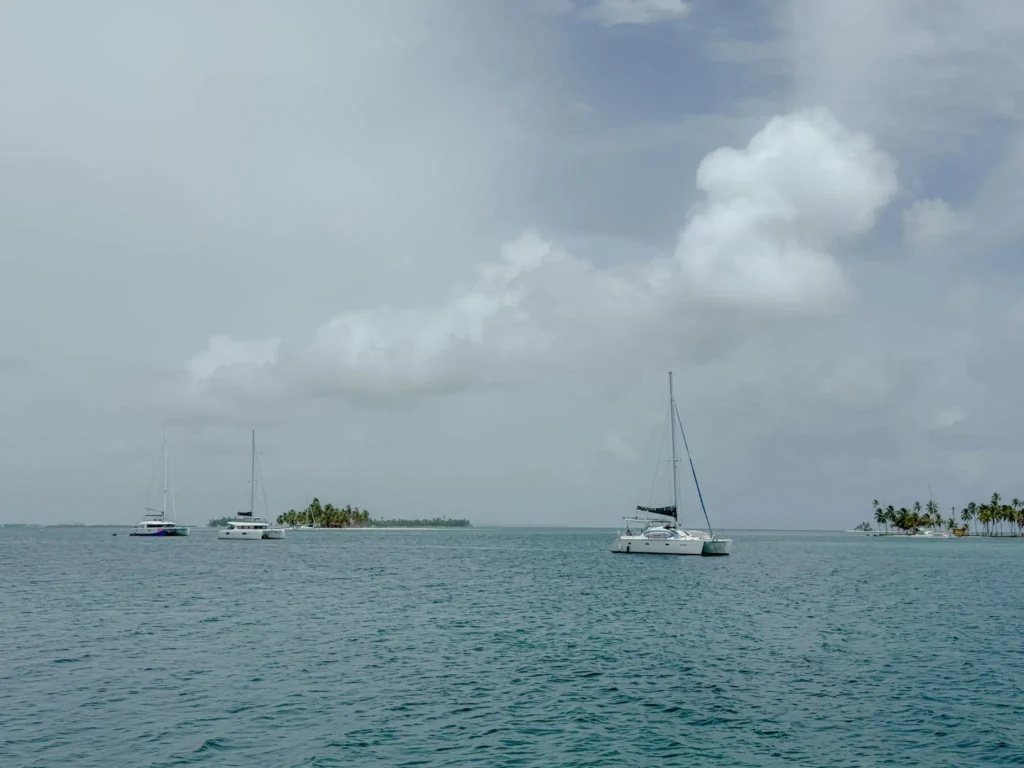 Catamarans anchored in the San Blas archipelago with a palm-covered island in the distance — day trips from Panama City