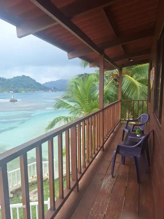Wooden balcony at Cabanas Blue with two chairs overlooking turquoise water and palms on Isla Grande -- Portobelo Panama
