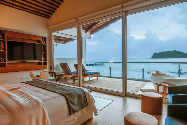 Interior of an overwater bungalow at Ordovician Beach Resort with floor-to-ceiling glass doors opening to the Caribbean sea at dusk -- Portobelo Panama