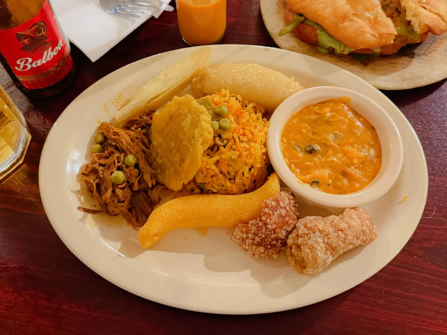 A plate of traditional Panamanian food with ropa vieja, arroz con pollo, patacones, and a Balboa beer bottle - Panama food guide