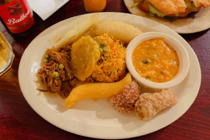A plate of traditional Panamanian food with ropa vieja, arroz con pollo, patacones, and a Balboa beer bottle - Panama food guide