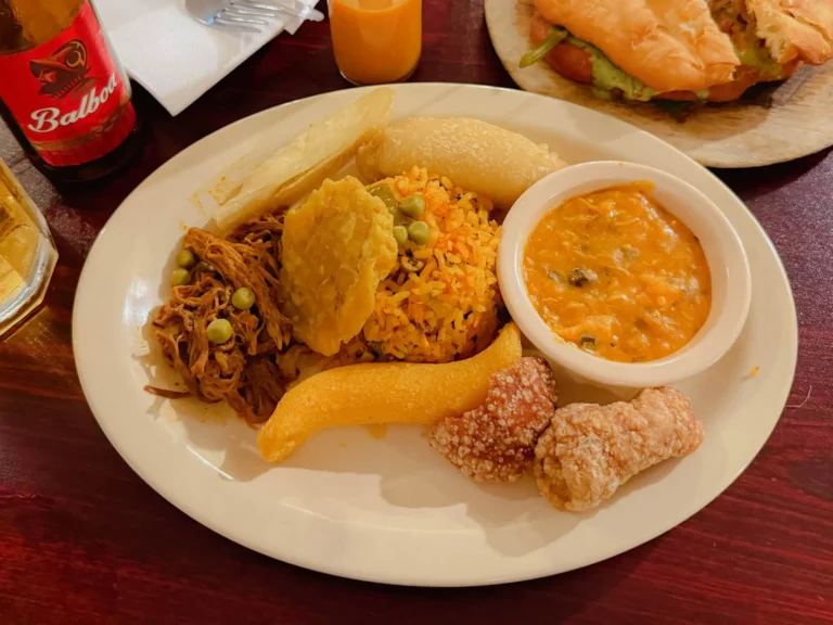 A plate of traditional Panamanian food with ropa vieja, arroz con pollo, patacones, and a Balboa beer bottle - Panama food guide