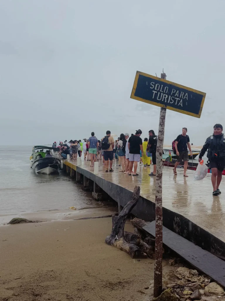 Travelers boarding boats at the Carti dock on a rainy day with a Solo Para Turista sign in the foreground -- San Blas sailing embarkation Carti dock Panama