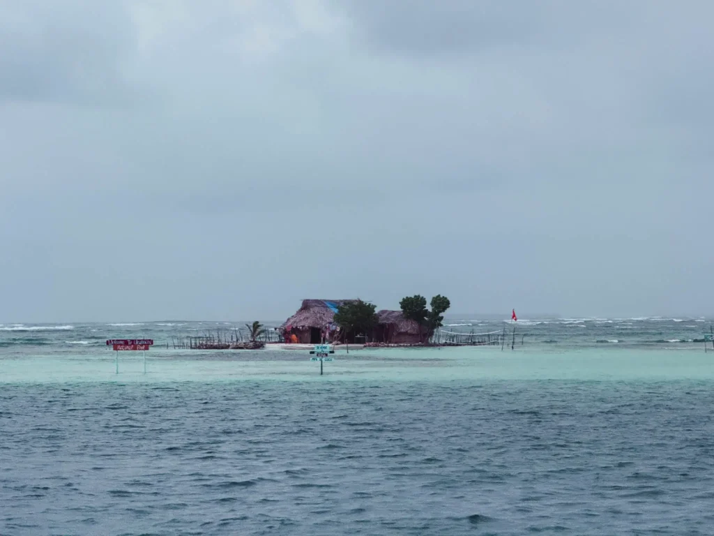 A small Guna island with thatched huts visible from the water on an overcast day with choppy grey seas -- rainy season San Blas Islands Panama