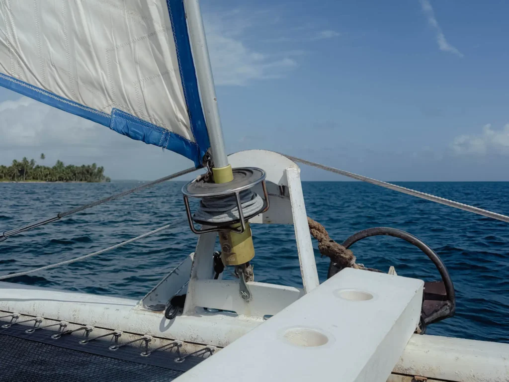View from the bow of a sailing catamaran underway with a white sail and a palm-covered San Blas island in the distance -- sailing San Blas Islands Panama