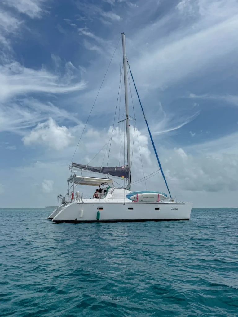 A white sailing catamaran named Serenita anchored in open turquoise water under a partly cloudy sky -- San Blas sailing catamaran
