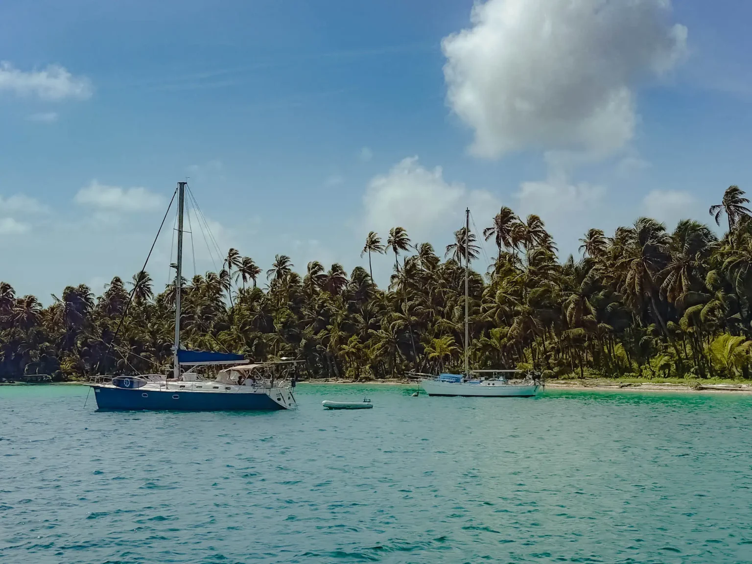 Two sailboats anchored in turquoise water beside a dense palm-covered island in the San Blas archipelago -- sailing San Blas Islands Panama