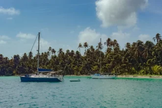 Two sailboats anchored in turquoise water beside a dense palm-covered island in the San Blas archipelago -- sailing San Blas Islands Panama