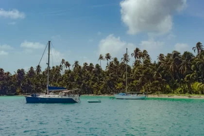 Two sailboats anchored in turquoise water beside a dense palm-covered island in the San Blas archipelago -- sailing San Blas Islands Panama