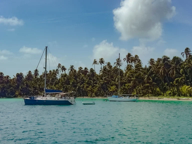 Two sailboats anchored in turquoise water beside a dense palm-covered island in the San Blas archipelago -- sailing San Blas Islands Panama