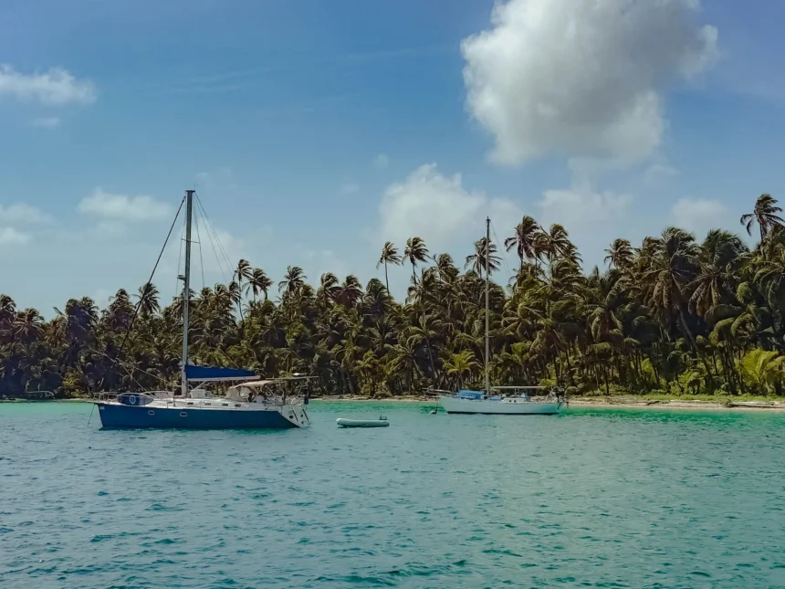 Two sailboats anchored in turquoise water beside a dense palm-covered island in the San Blas archipelago -- sailing San Blas Islands Panama