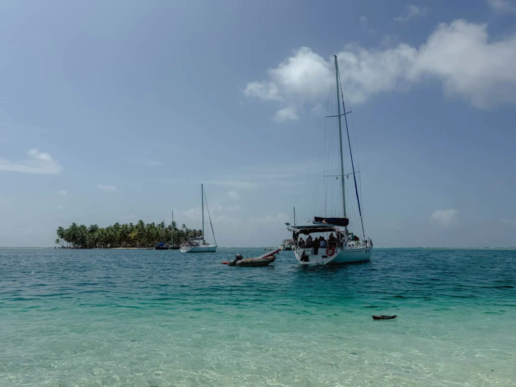 Two monohull sailboats anchored in calm turquoise water off a palm-covered San Blas island seen from the beach -- monohull sailing San Blas Islands