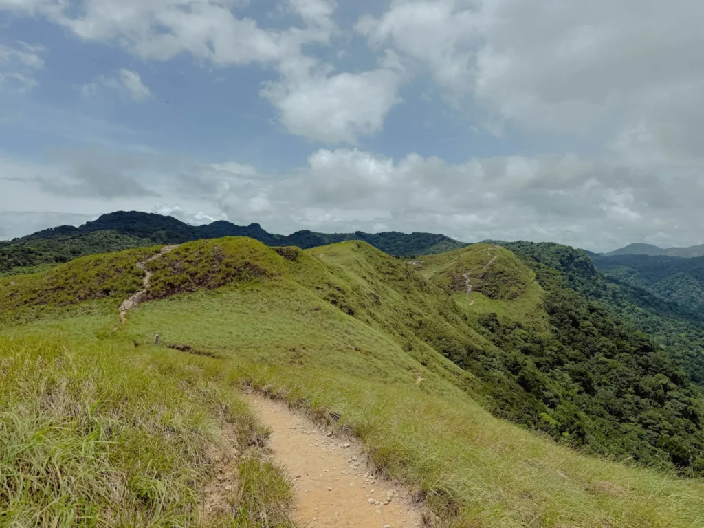 Exposed grassy ridge trail winding between two green peaks with dense forest dropping away on both sides - Valle de Anton hiking