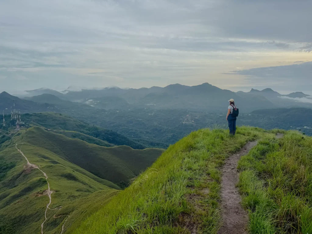 Hiker standing alone on the narrow La Silla ridge looking out over layered mountain ranges fading into morning mist above Valle de Anton - Valle de Anton hiking