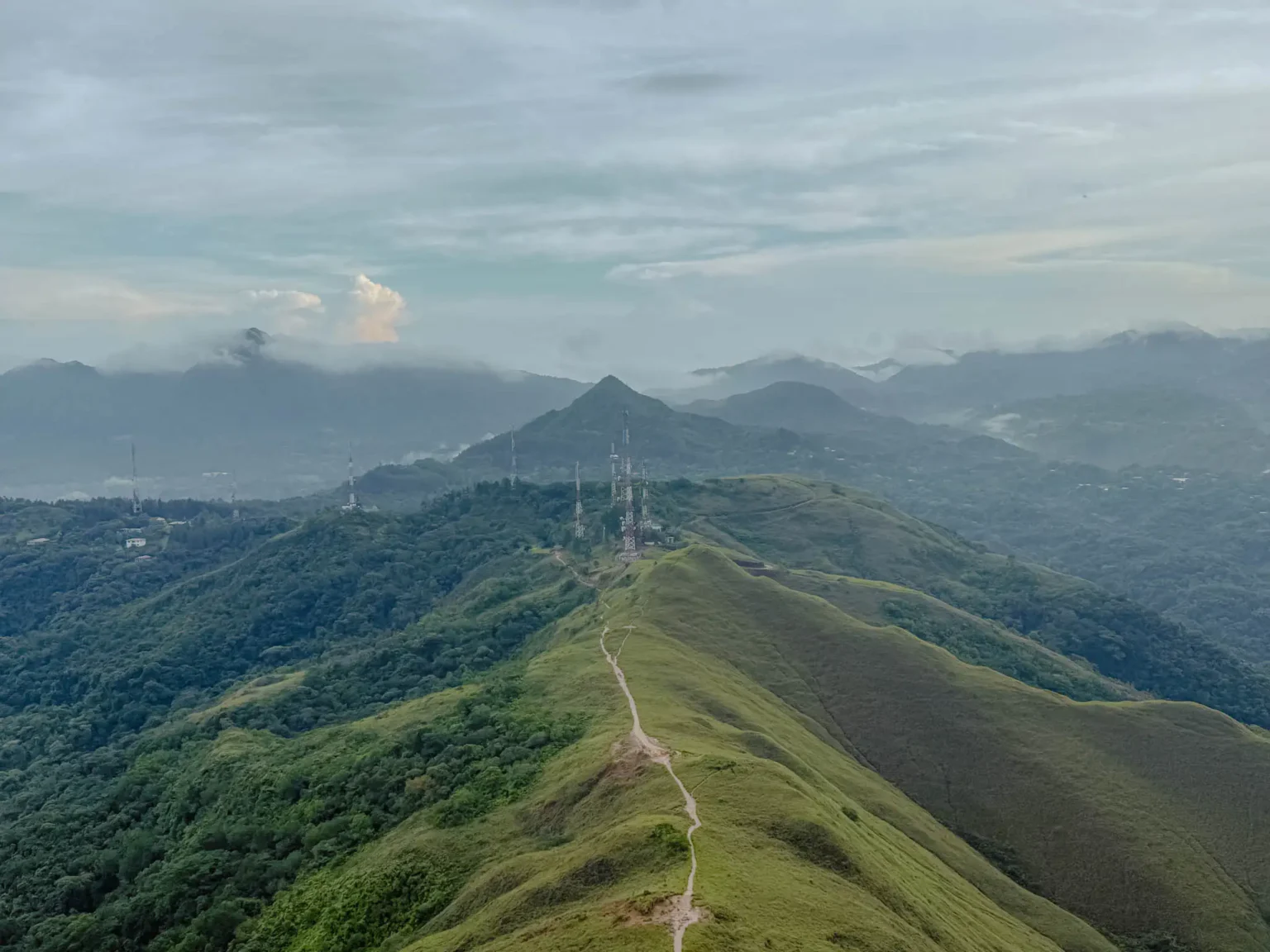 Aerial view of the Valle de Anton crater ridgeline with a trail running along the spine and mist-covered mountains in the background -- Valle de Anton Panama