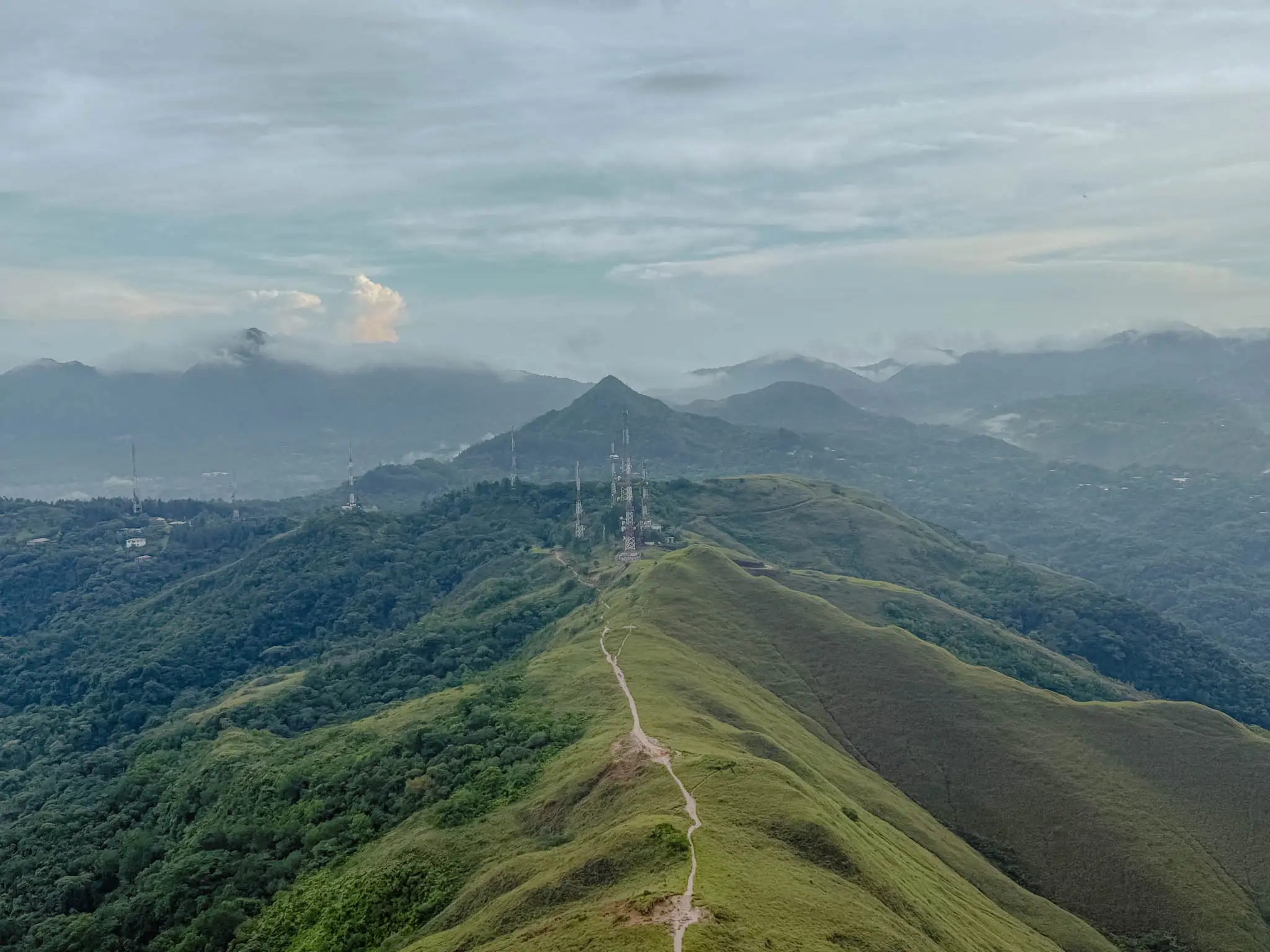 Aerial view of the Valle de Anton crater ridgeline with a trail running along the spine and mist-covered mountains in the background -- Valle de Anton Panama