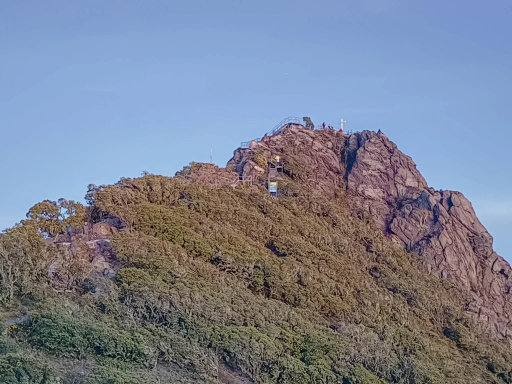 The cross marking the true summit of Volcan Baru with hikers visible at the top - Volcan Baru hike