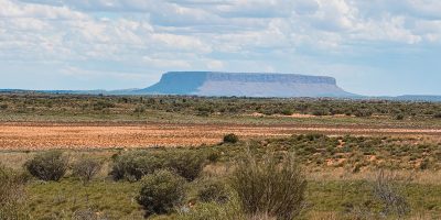 A flat topped large rock behind a large field - 3 day uluru tour