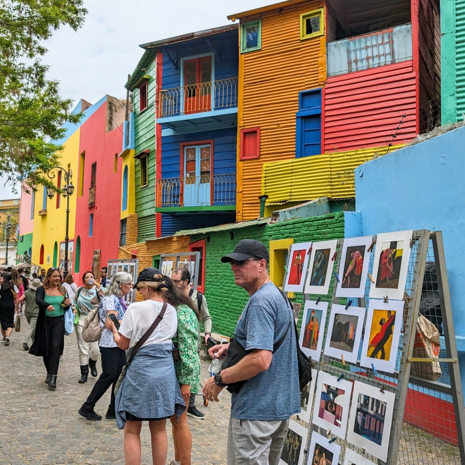 People walking down a pedestrian walkway with colorful buildings on the side and artist vendors on the walkway - free Buenos Aires walking tours