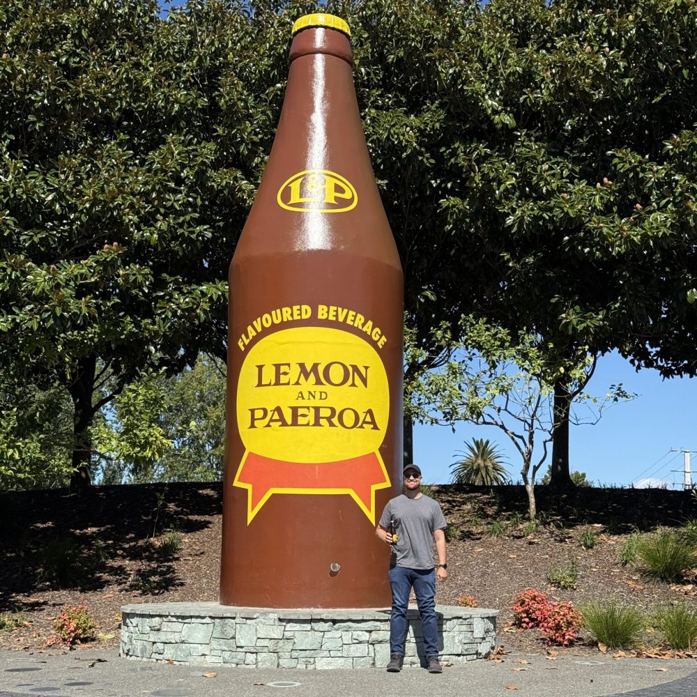 A man standing in front of a giant brown soda bottle outside of Auckland, New Zealand