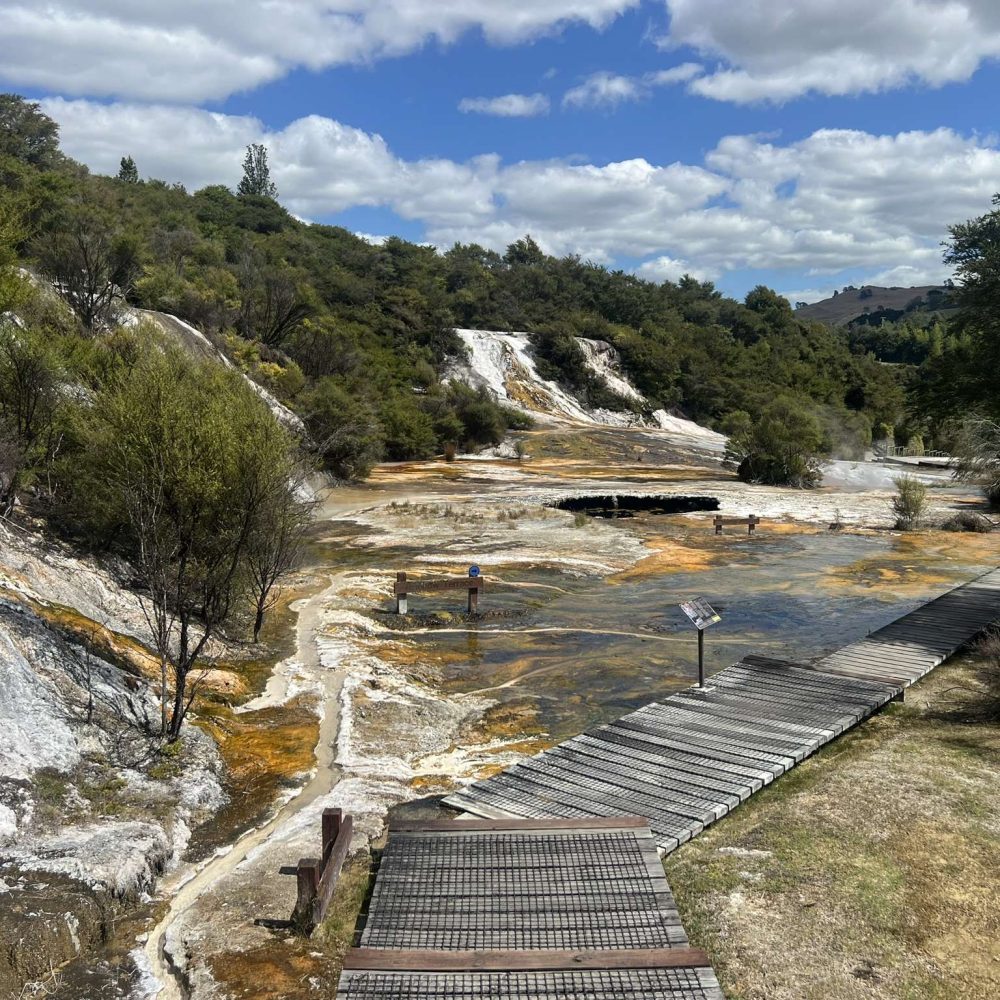 The landscape of a geothermal area near the Tongariro Crossing with a boardwalk running over the orange and yellow rocks and a good way to compare the south island vs north island