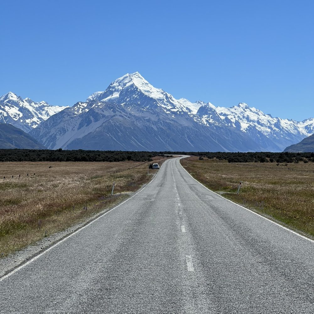 New Zealand-Mount Cook-Christchurch-Dunedin-10 A road leading to a large white-capped mountain on a trip from Christchurch to Dunedin