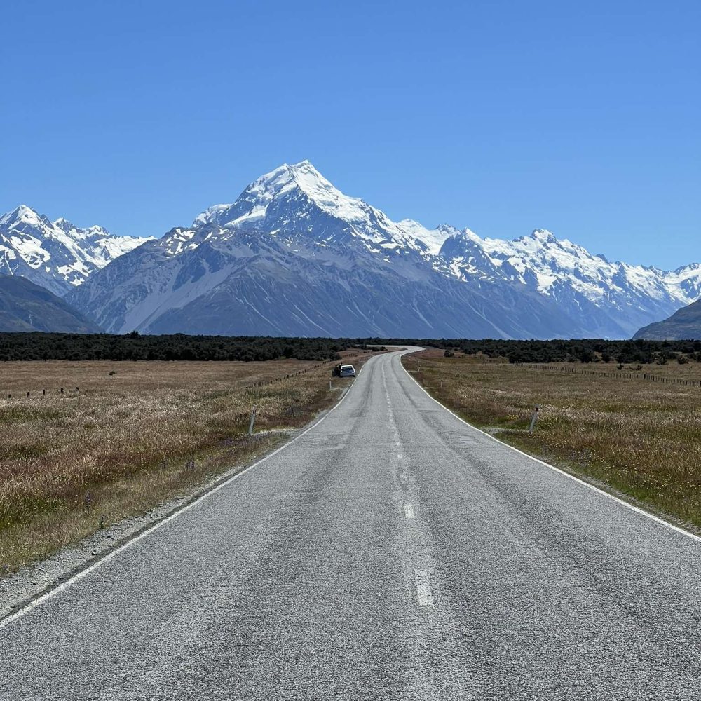 A road leading to a large white-capped mountain on a trip from Christchurch to Dunedin