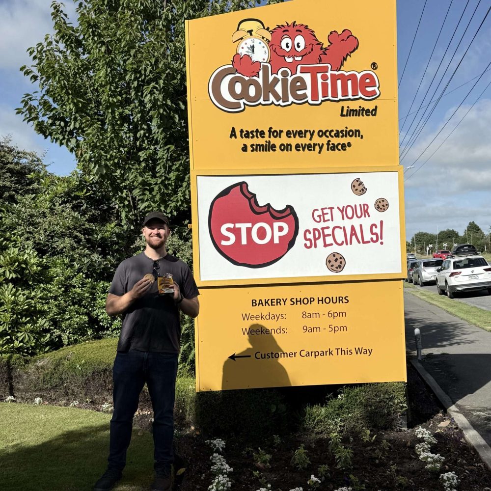 A man standing in front of a sign on a trip from Christchurch to Dunedin