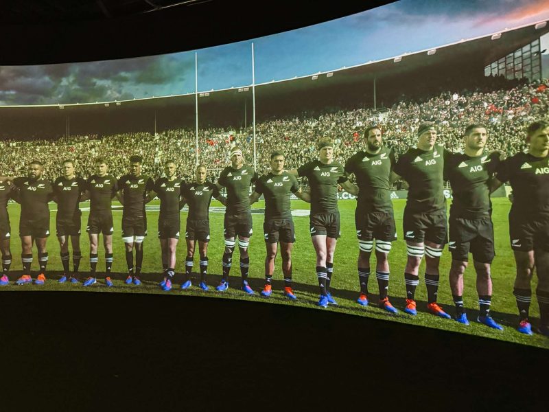 People linked arms in a line on a panoramic screen part of an Auckland itinerary for a weekend in Auckland