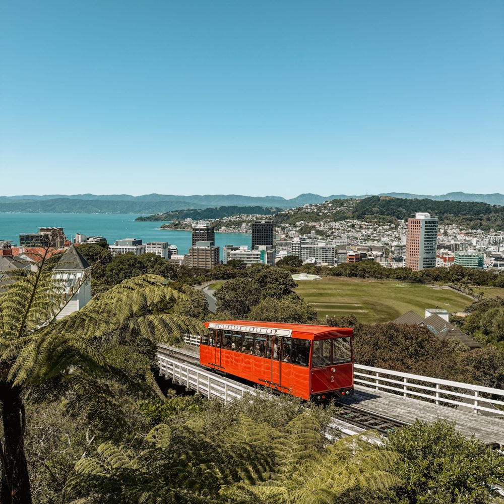 New Zealand-North Island-Wellington-17 A red cable car going up a hill with a bay in the background in Wellington